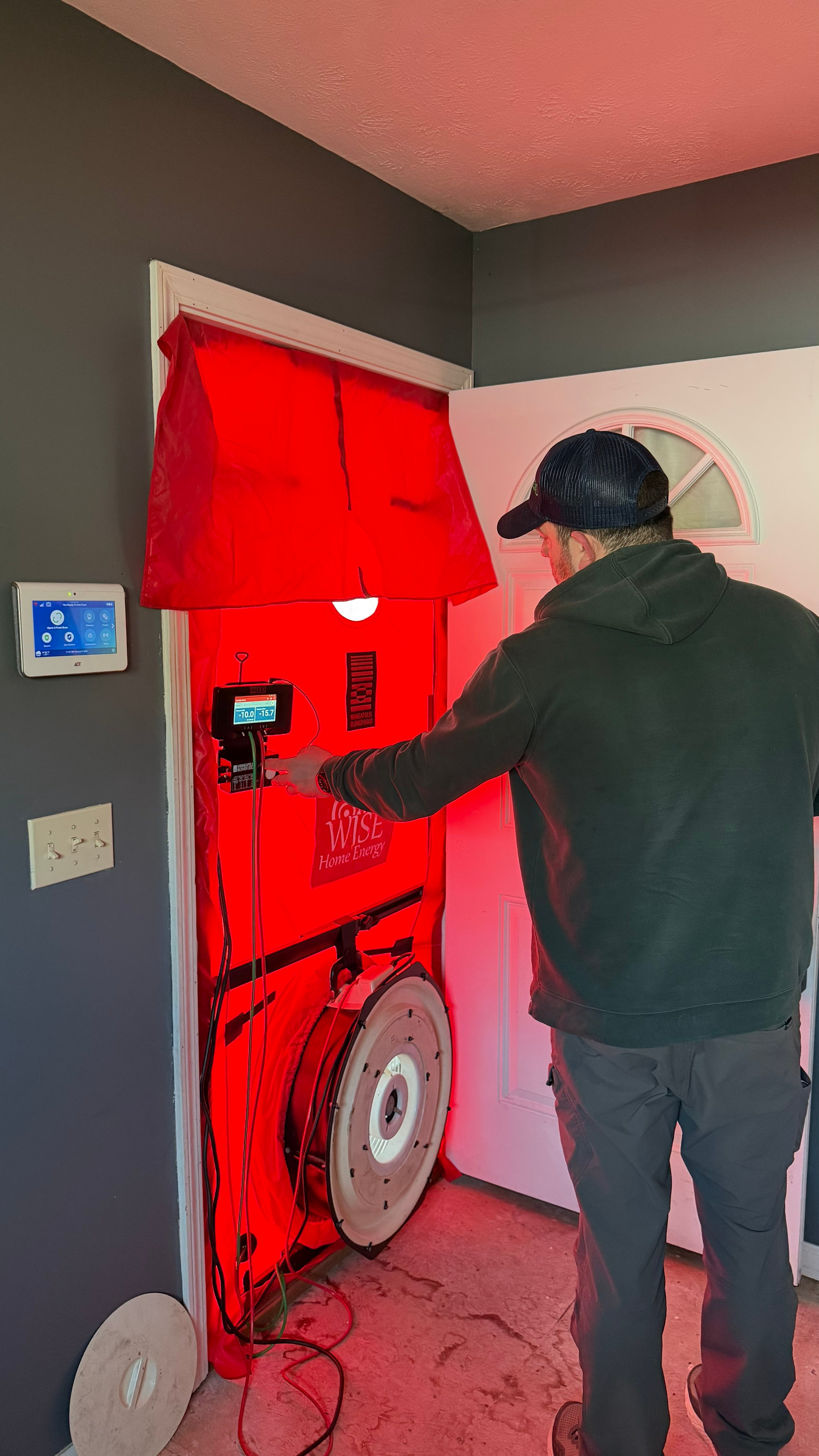 A Wise Home Energy building analyst standing in front of a blower door while performing a test on a home.